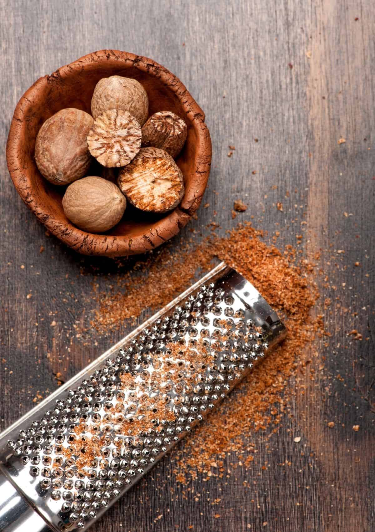 Nutmeg  in small wood bowl, beside ground nutmeg. - foods that start with n