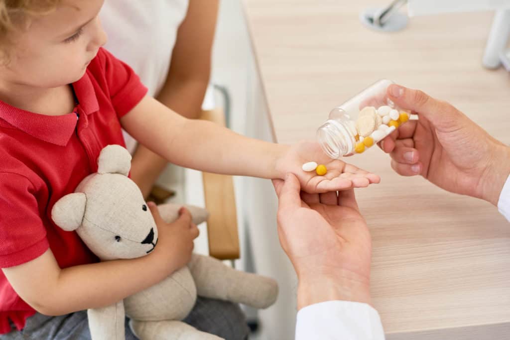 best kids vitamin for brain development - Closeup of unrecognizable doctor giving vitamins to curly little boy during appointment