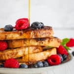 A stack of healthy french toast with berries and maple syrup drizzling on top.