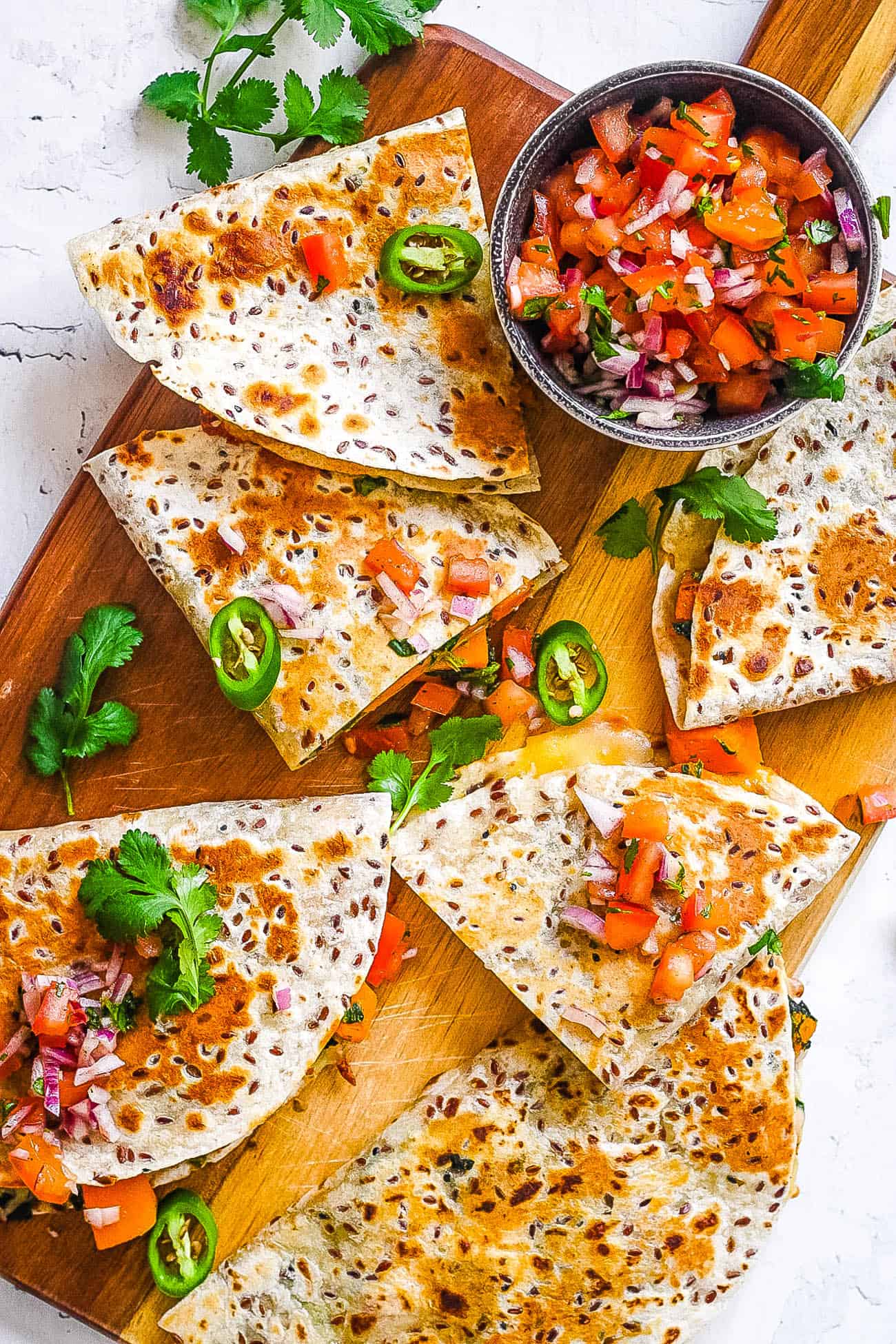 vegan quesadillas made with butternut squash and kale topped with pico de gallo on a cutting board