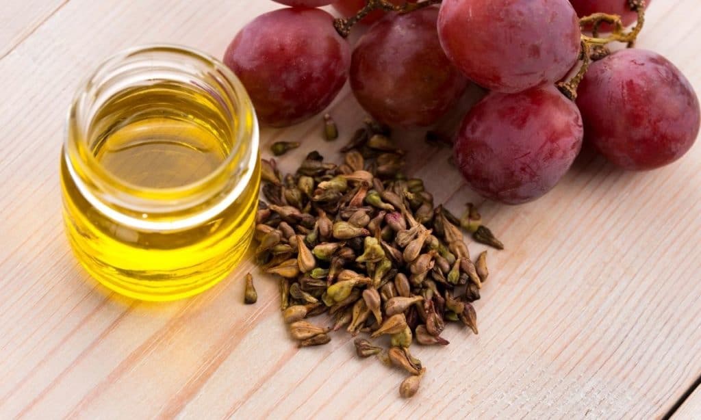 Grapeseed oil in small jar beside pile of grapeseeds and red grapes. - best oil to season cast iron