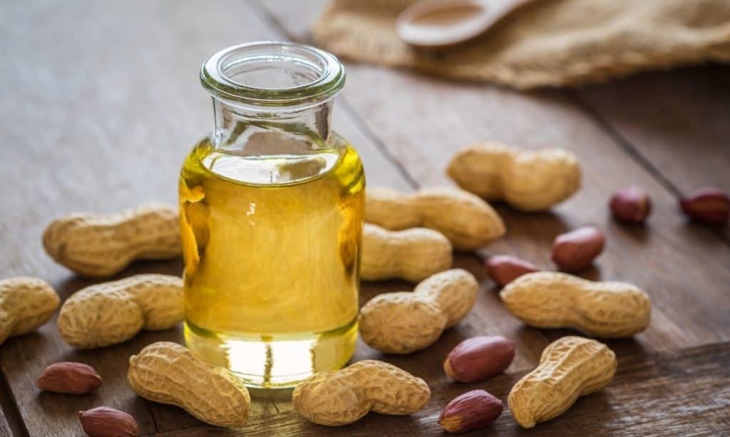 Peanut oil in small jar, surrounded by peanuts and peanut shells.