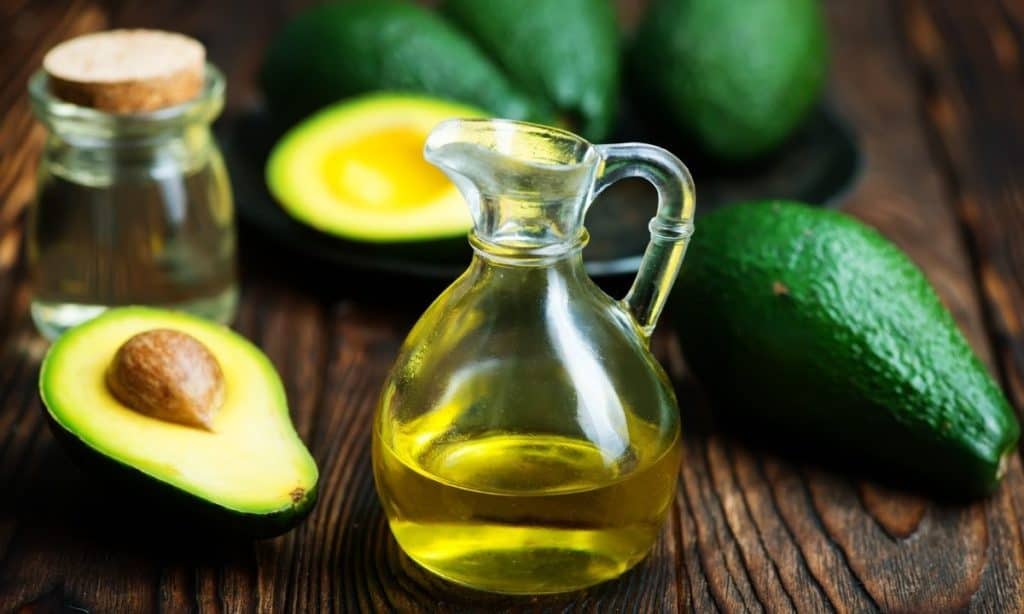 Avocado oil in small pouring jar, surrounded by fresh avocadoes.