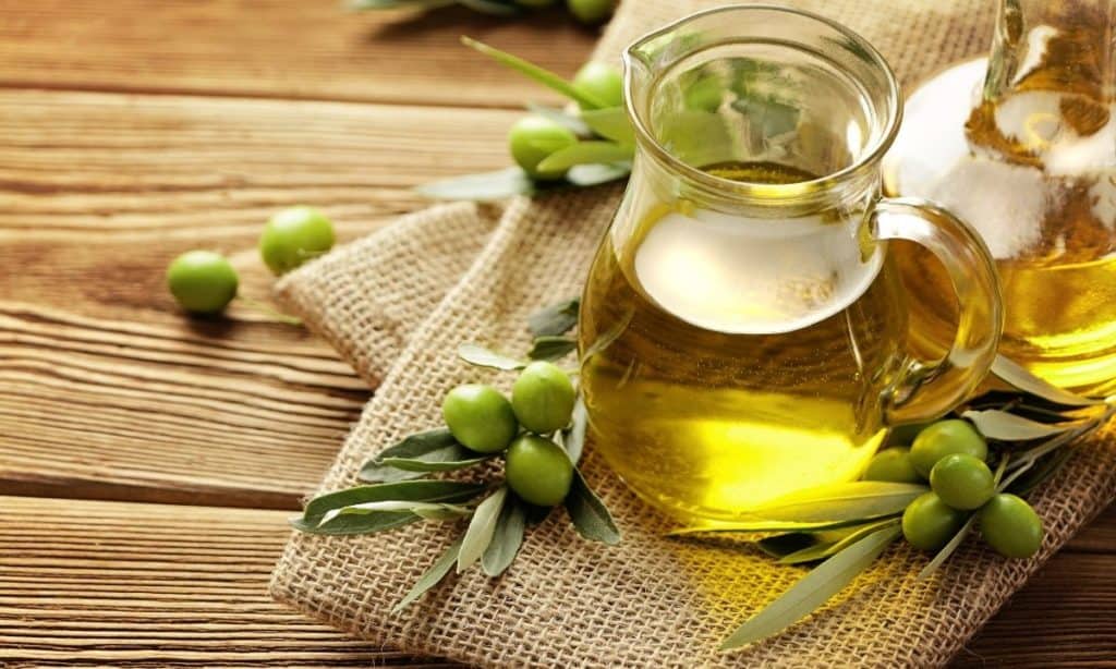 Olive oil in small pitcher surrounded by green olives. 