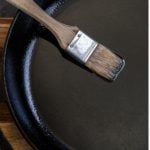 Cast iron skillet coated with cooking brush coated in oil.