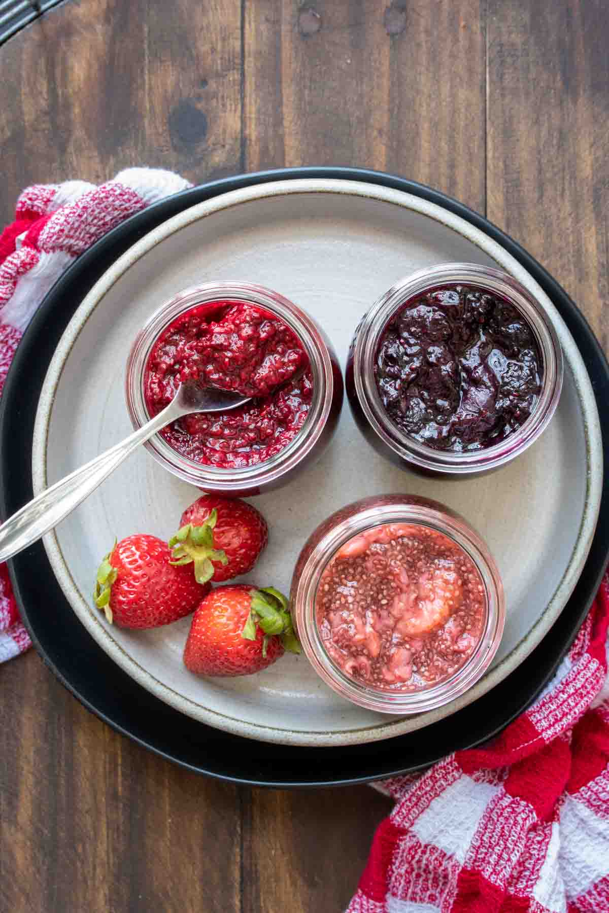 Top view of a plate with three jars on it filled with different flavors of jam.