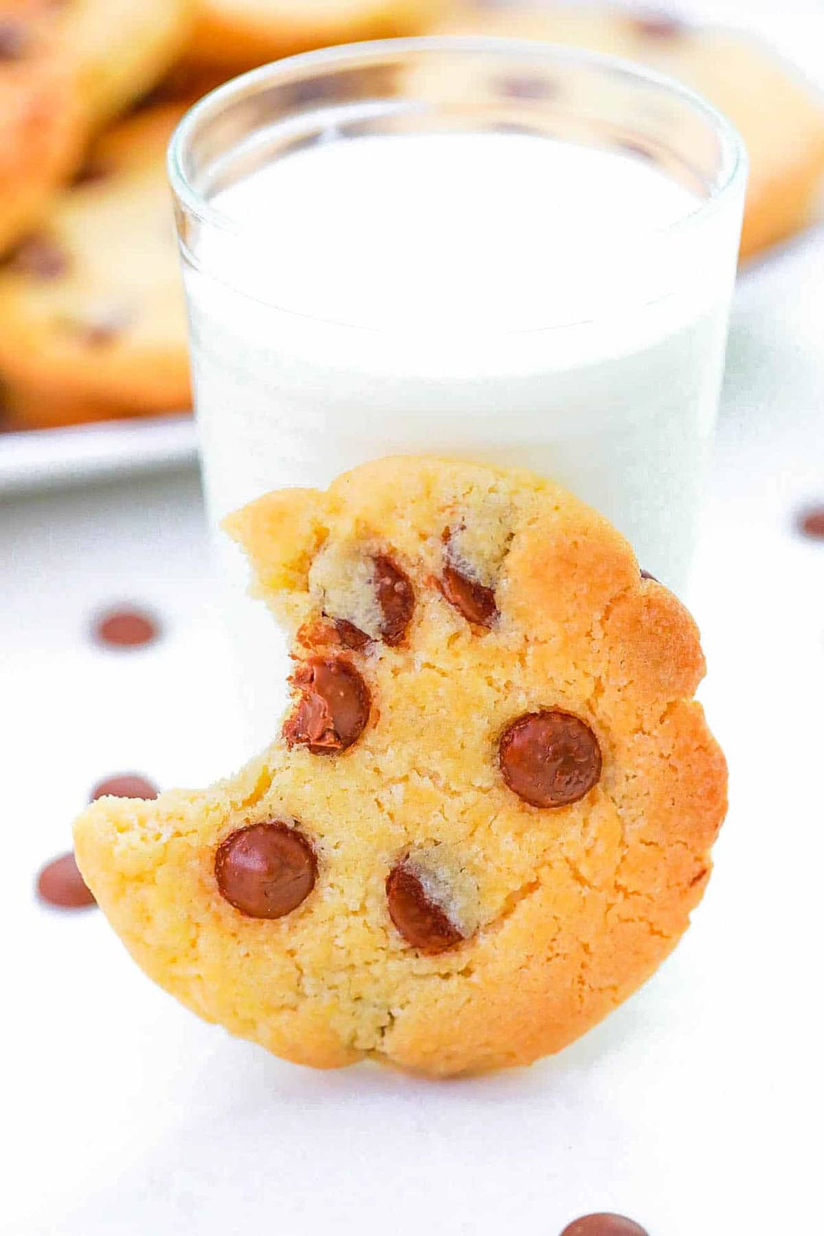 One chocolate chip cookie made without brown sugar propped up against a glass of milk with a bite taken out.