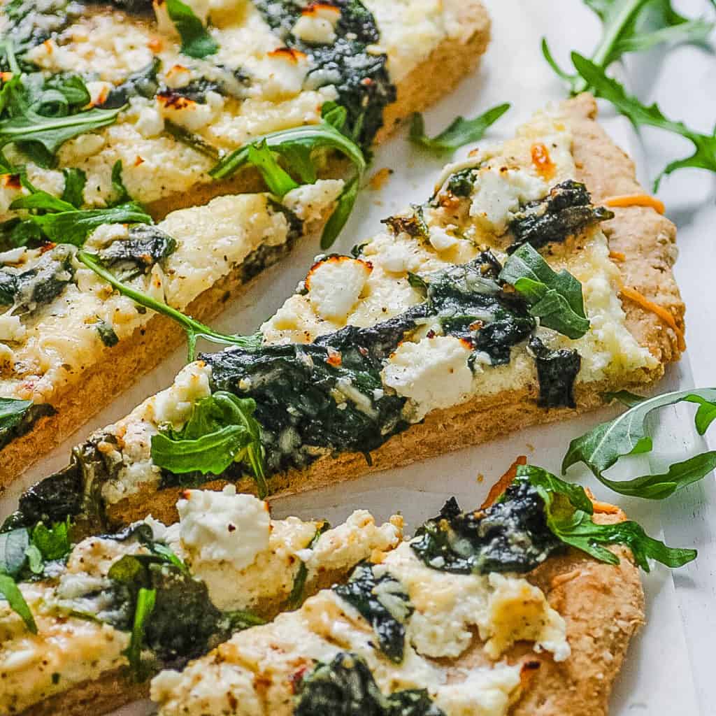 vegetarian florentine pizza - white pizza with spinach and parmesan cheese, sliced on a white platter