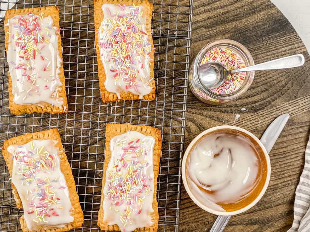healthy homemade vegan pop tarts with strawberry filling being iced with rainbow sprinkles and coconut yogurt icing