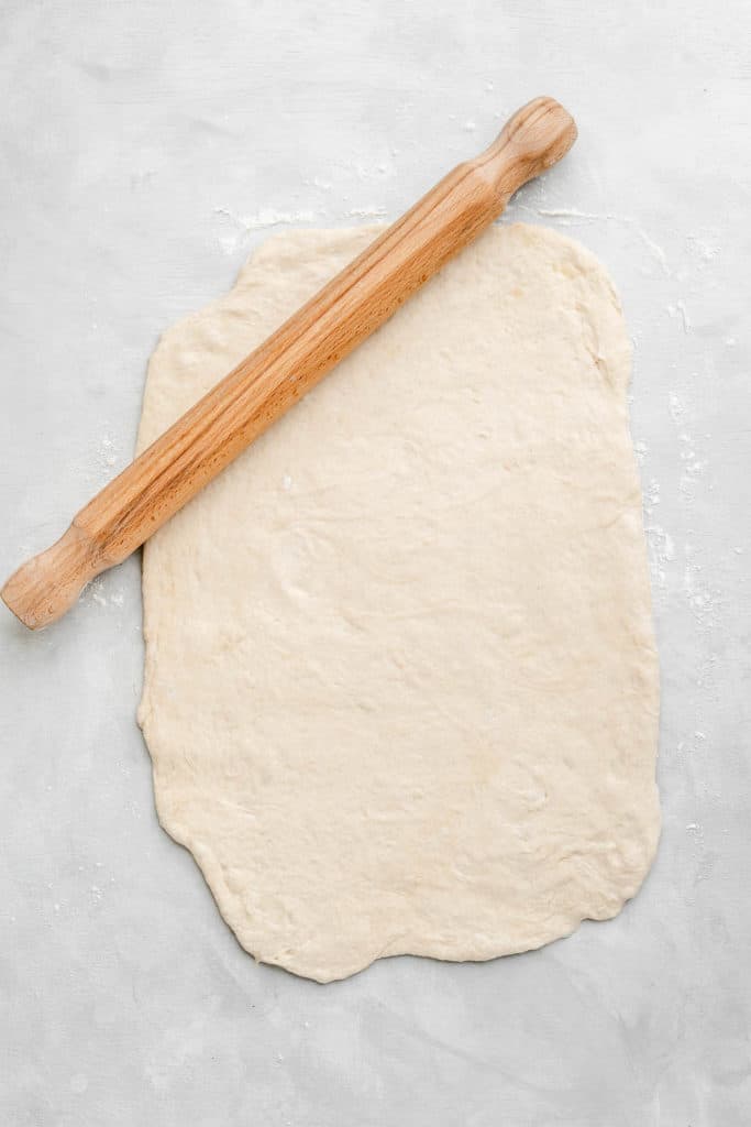 pizza dough being rolled out with a rolling pin