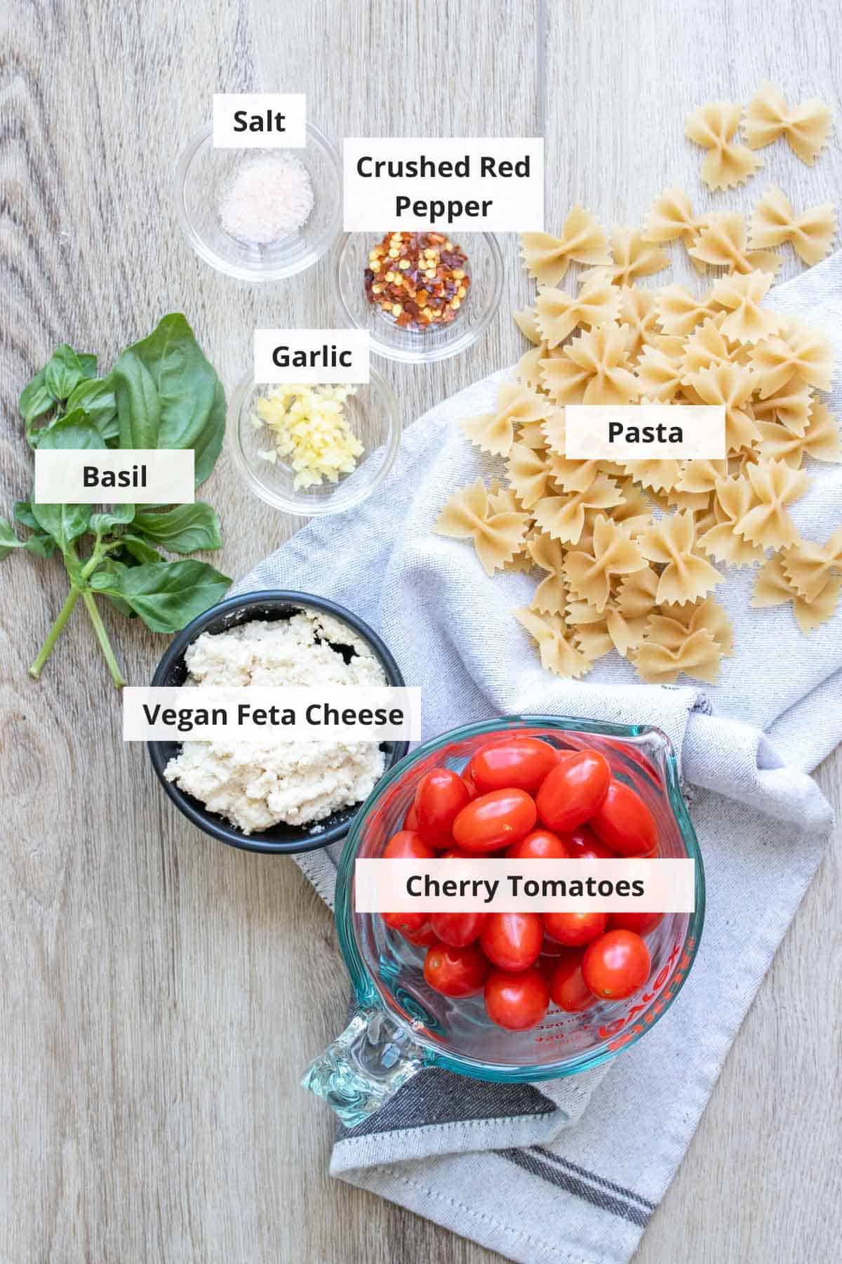 Ingredients for vegan baked feta pasta on a wood background.