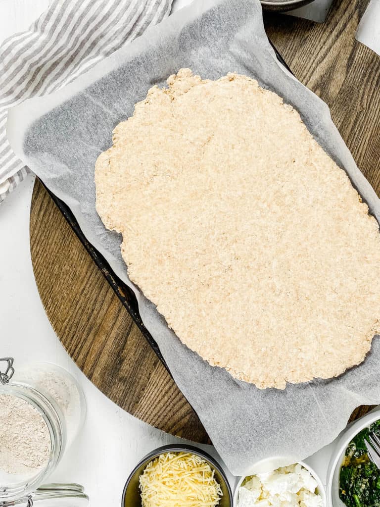 Pizza dough rolled out on parchment paper.