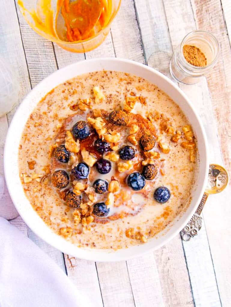 Pumpkin spice oatmeal with blueberries in a white bowl on a wooden countertop.