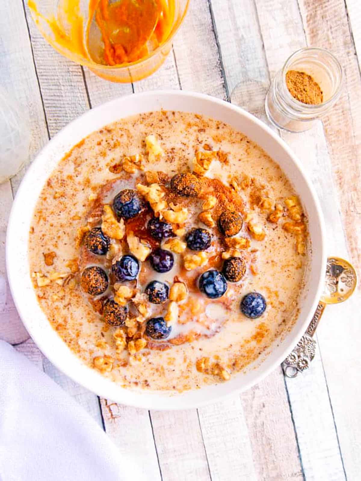 Pumpkin spice oatmeal with blueberries in a white bowl on a wooden countertop.