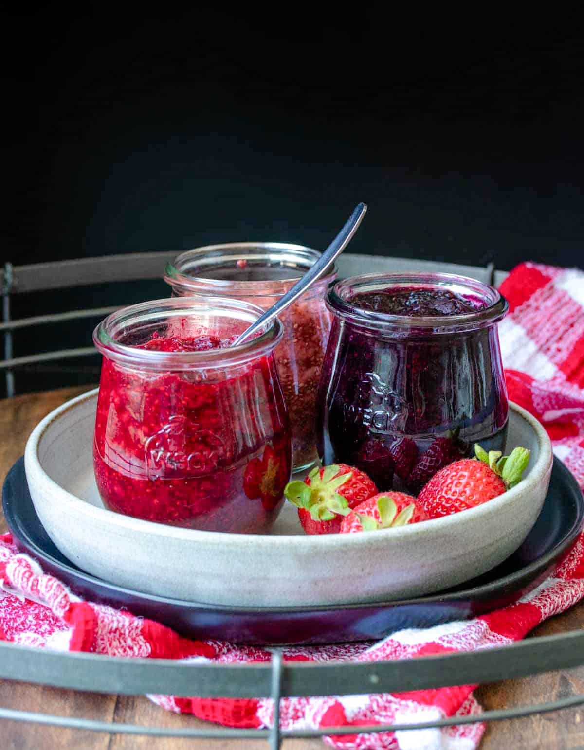 Front view of three jars filled with blueberry, raspberry and strawberry seed jam on a grey plate.