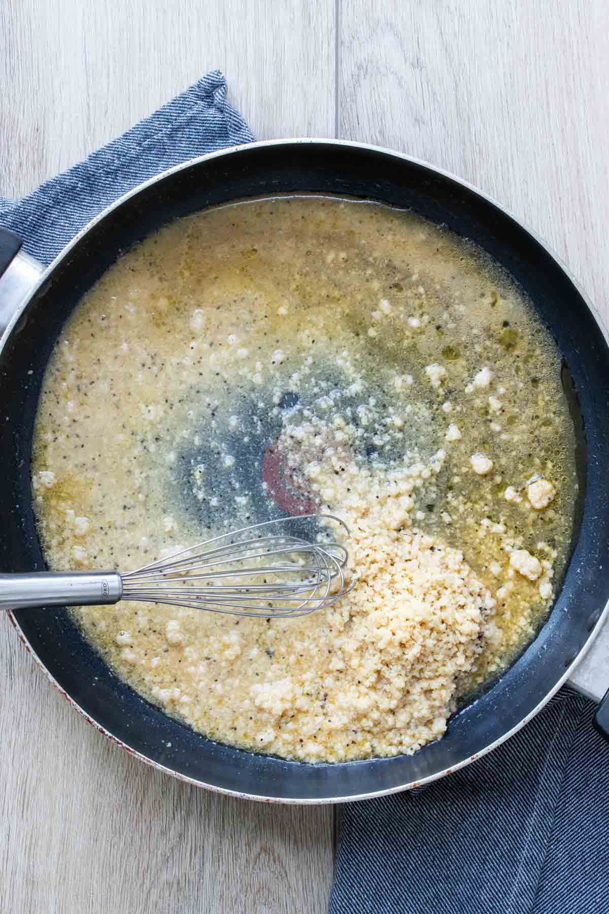 Whisk mixing vegan parmesan into broth + olive oil mixture.