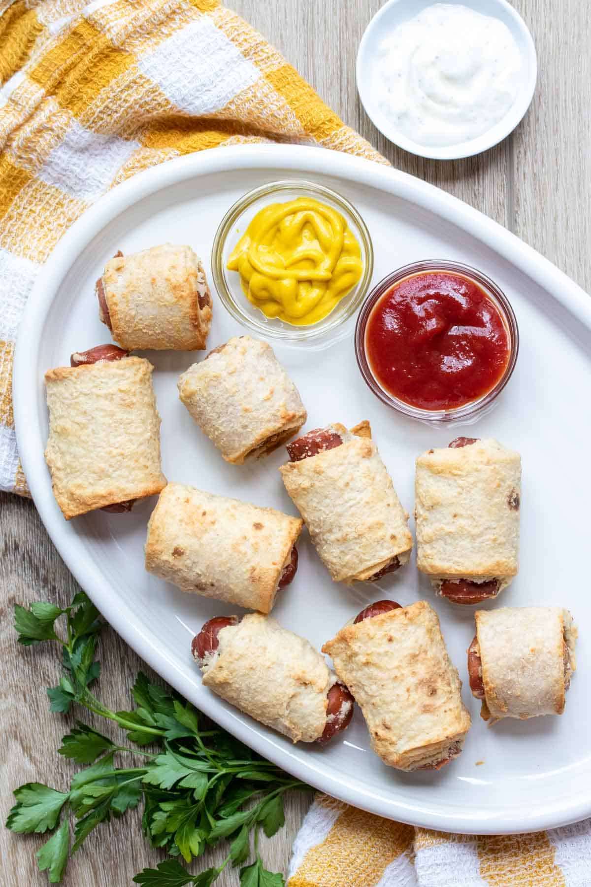 A white plate with ketchup and mustard in dipper jars and vegan pigs in a blanket.