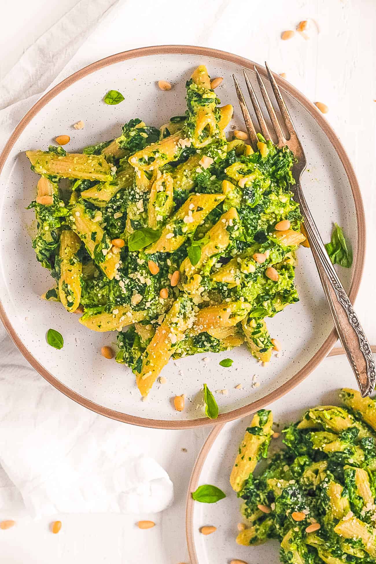 vegetarian pesto pasta recipe with spinach, basil and pine nuts on a white plate