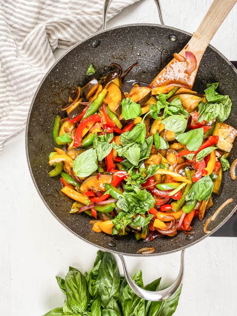 basil added to sauteed veggies and sauce in a wok.