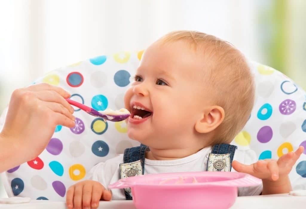 Happy baby in high chair eating oat cereal. 