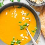 creamy butternut squash soup with coconut milk, cilantro and crushed nuts served in a black bowl