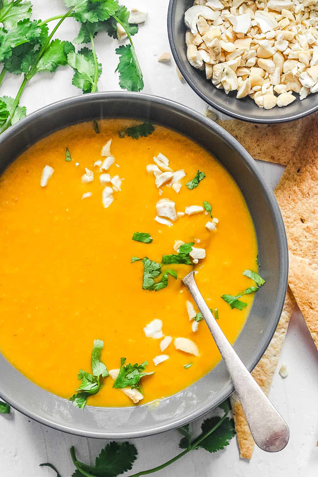 creamy butternut squash soup with coconut milk, cilantro and crushed nuts served in a black bowl