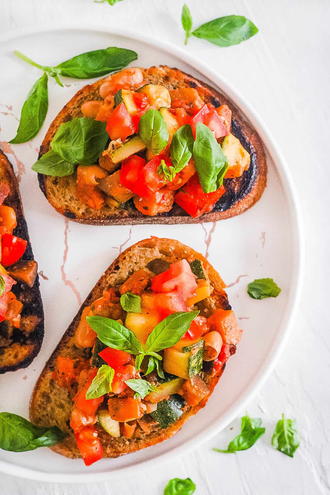 easy vegan bruschetta with tomatoes and white beans on a plate topped with basil