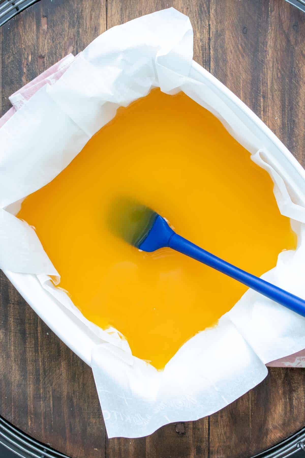 Blue spatula mixing an orange liquid in a white baking dish