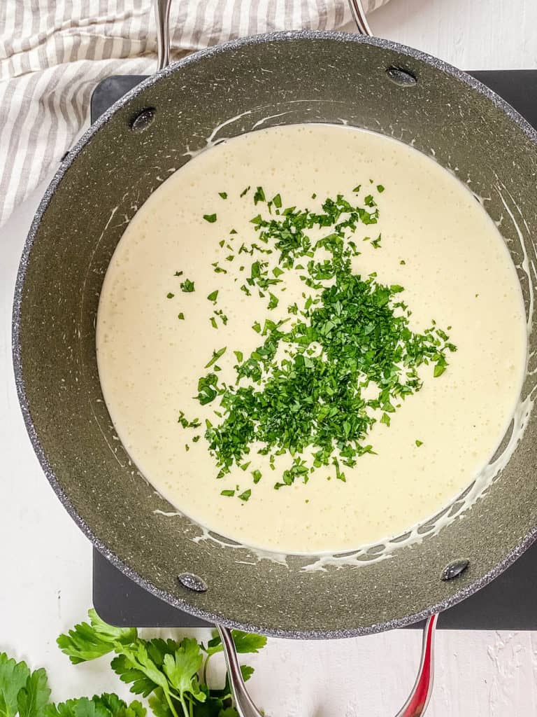 alfredo sauce without cream cooking in a pot with fresh parsley added
