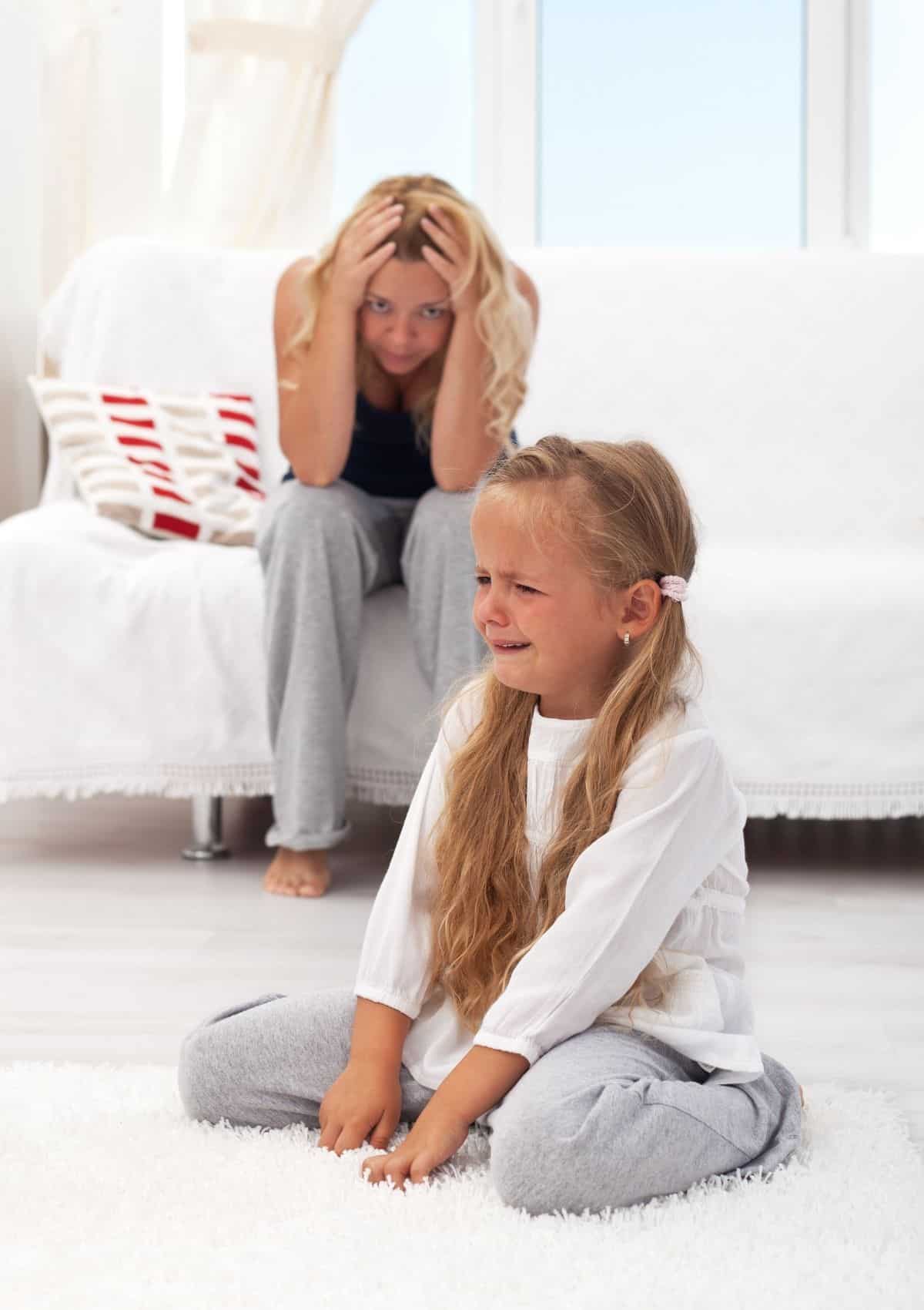 Mom with head in her hands as daughter has a tantrum on the floor.