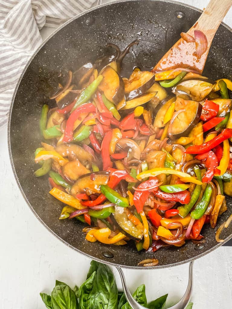 Sauteeing eggplant and peppers in the thai basil sauce in a wok.
