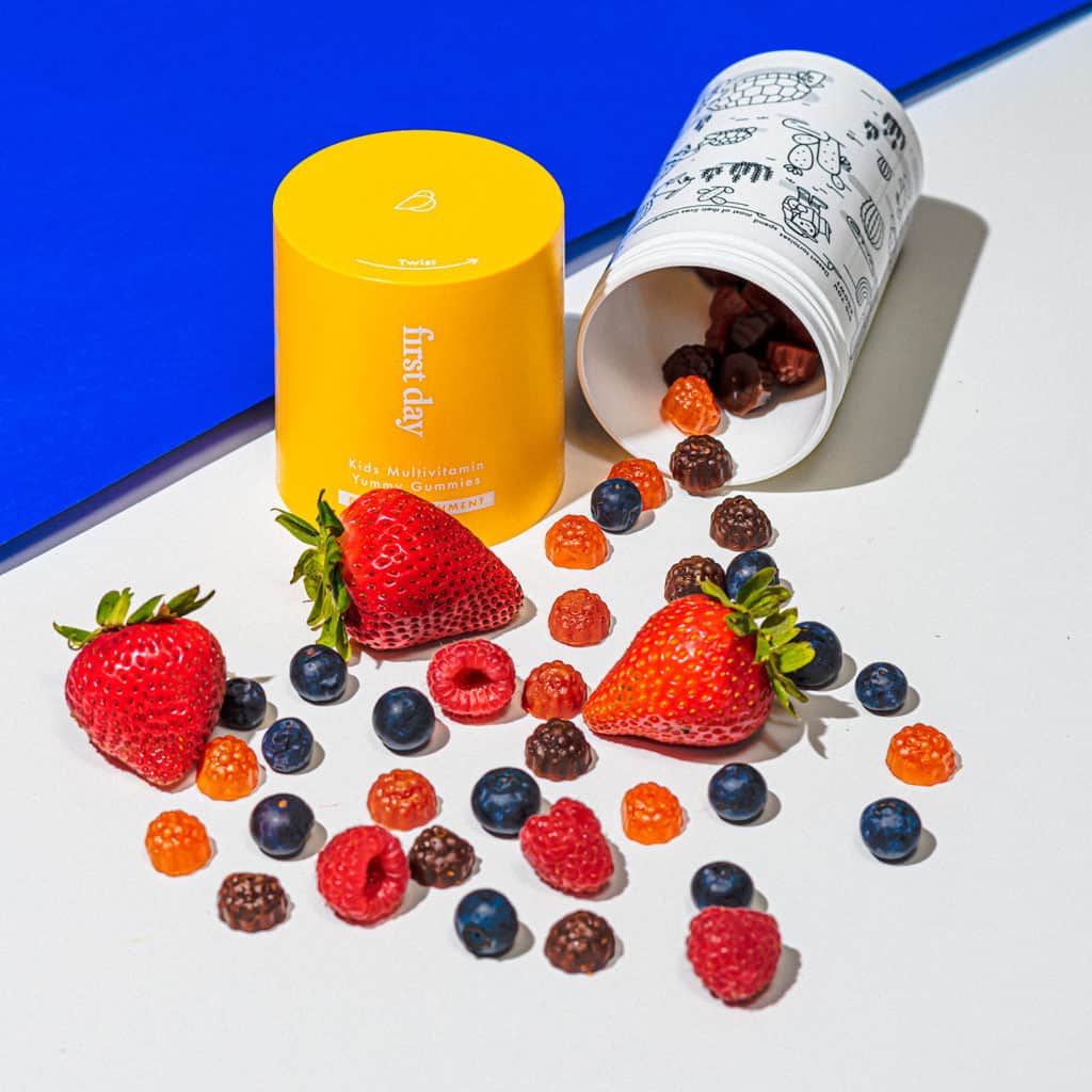 Bottle of first Day vitamins with gummies and berries rolling out. 
