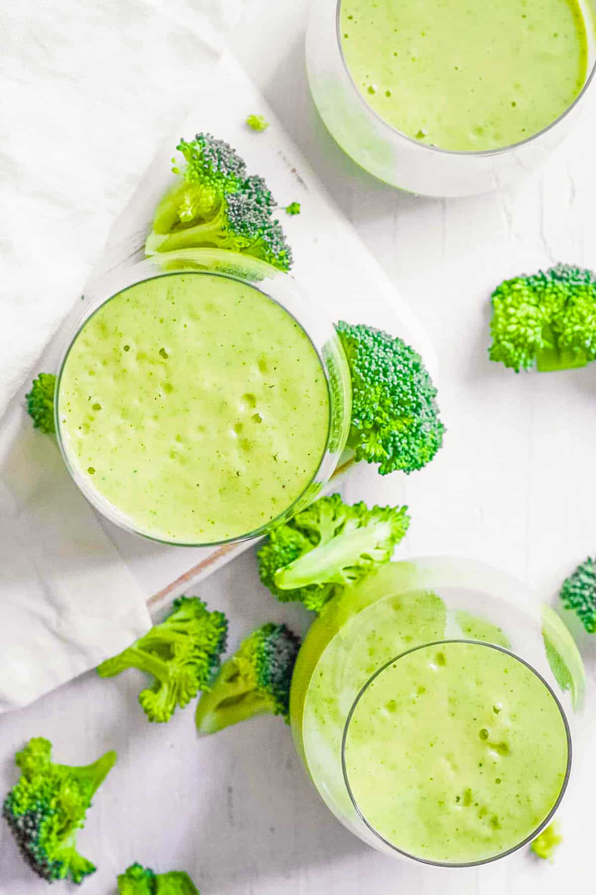 Healthy broccoli smoothie with banana in a glass on a white countertop.