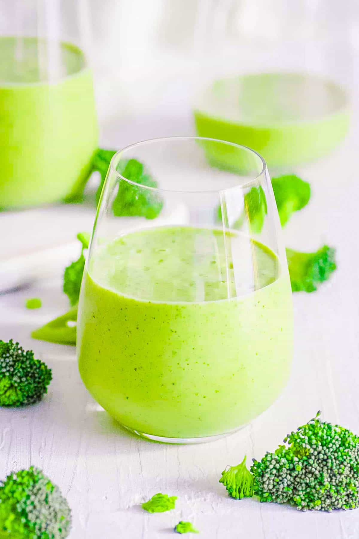 Healthy broccoli smoothie with banana in a glass on a white countertop.