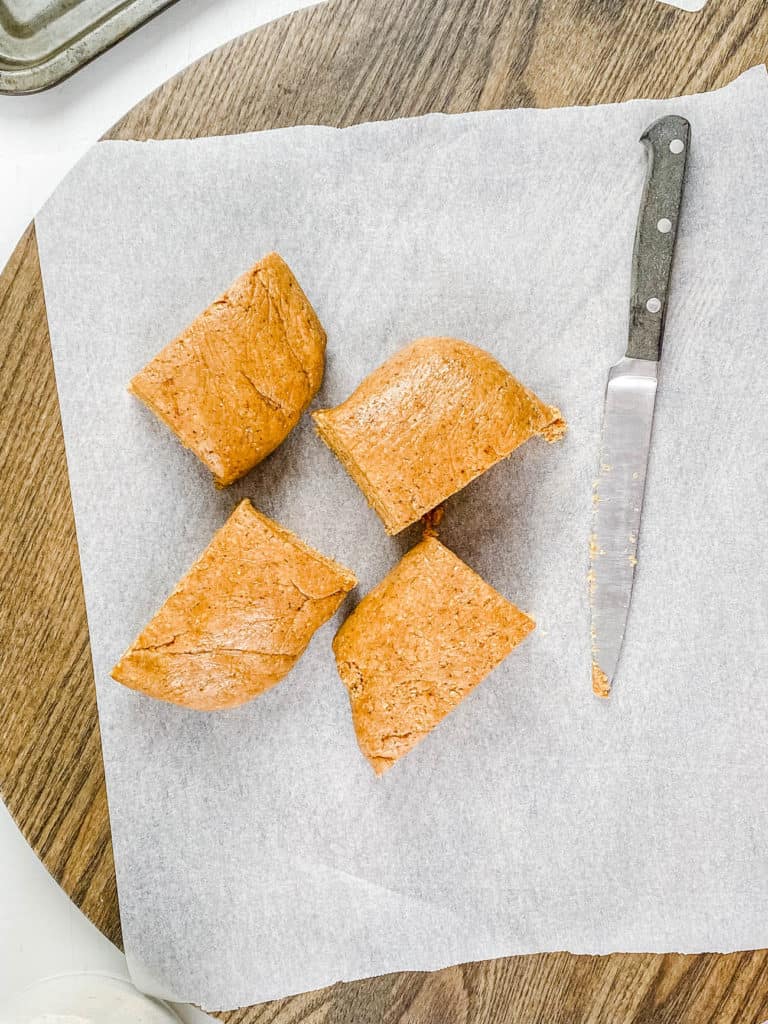 Vegan graham cracker dough cut into 4 pieces on parchment paper.