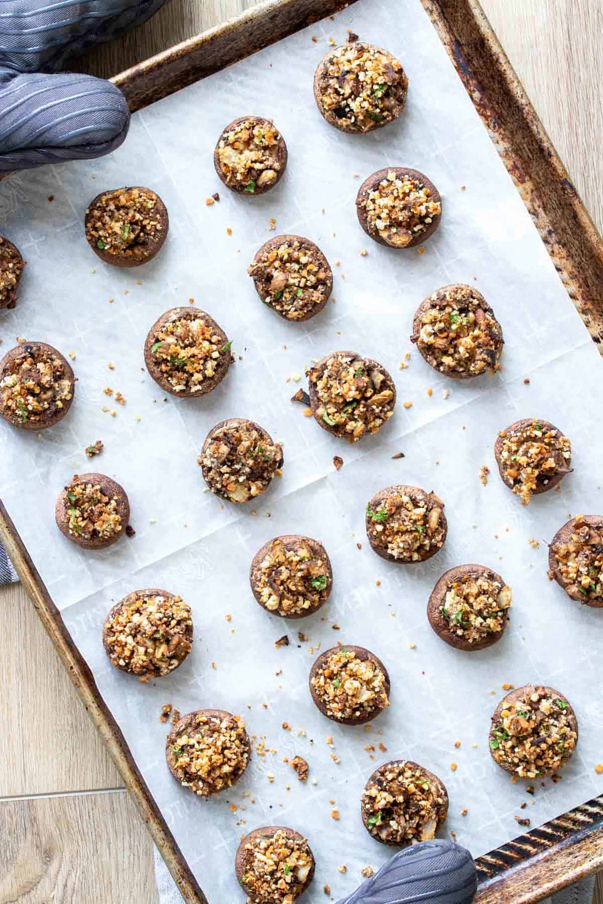 Top view of a parchment lined baking sheet filled with baked stuffed appetizer mushrooms