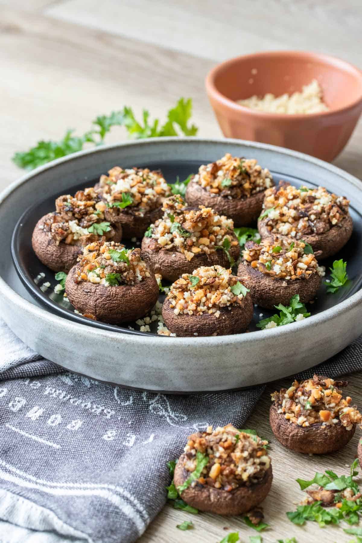 A black plate in a grey plate on a darker grey towel with stuffed appetizer mushrooms in it