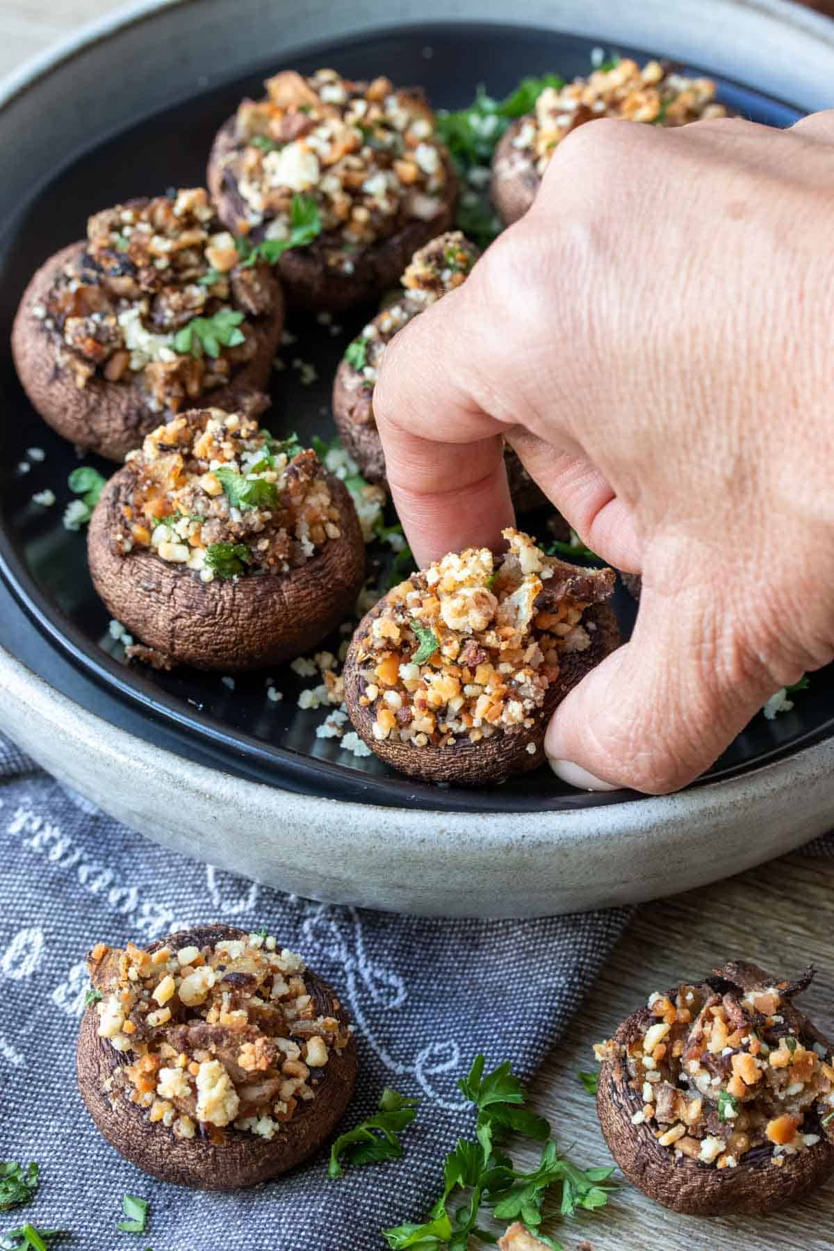 Hand grabbing a stuffed mushroom from a grey plate full of them