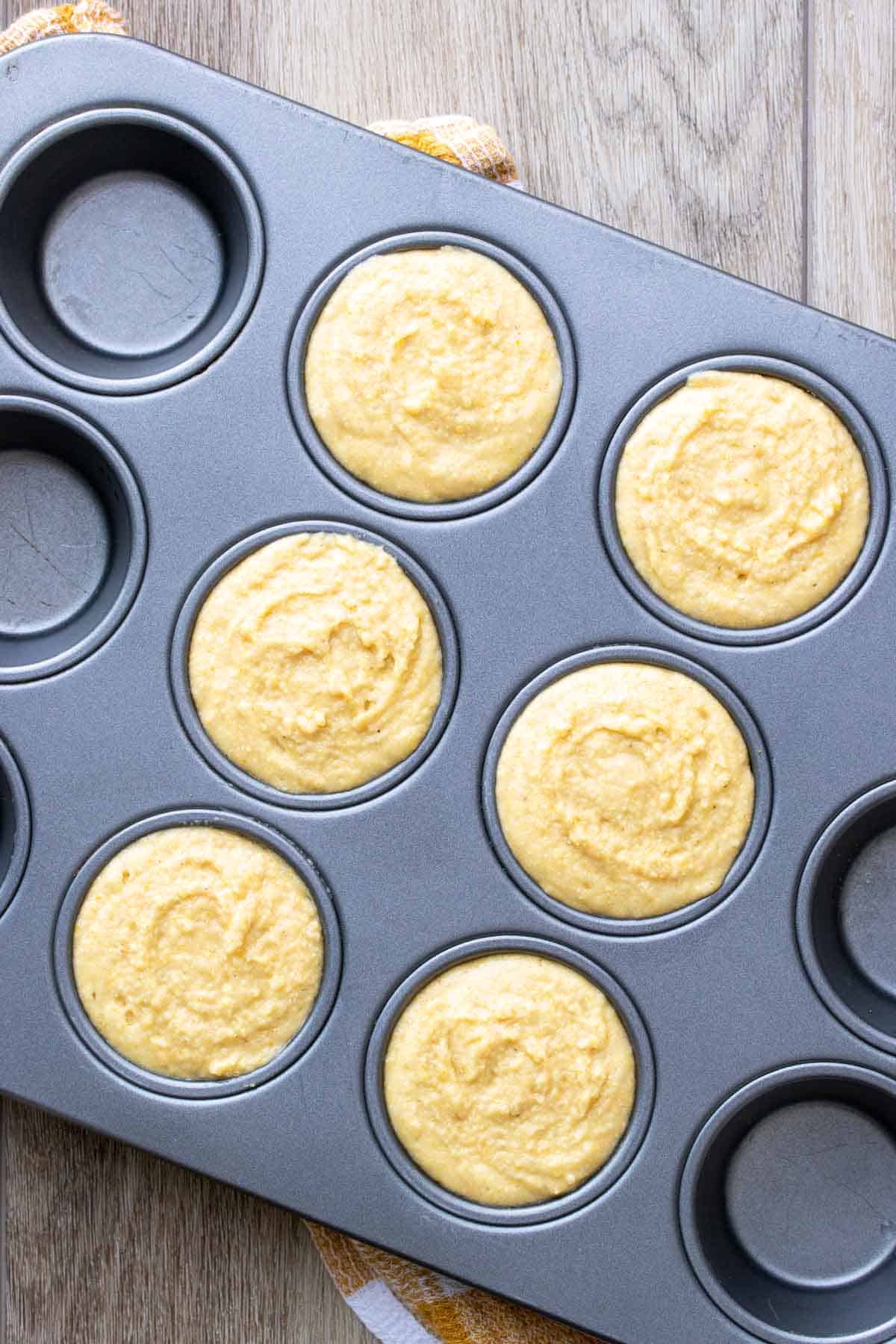 Muffin tin on a wooden surface filled with
vegan cornbread batter.