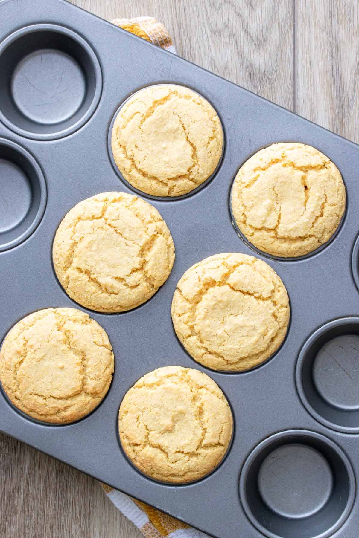Baked vegan cornbread muffins in a muffin tin sitting on a wooden surface.