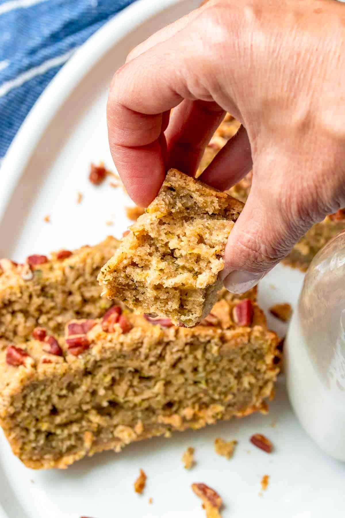 Hand picking up a slice of gluten-free vegan zucchini bread off of a plate.