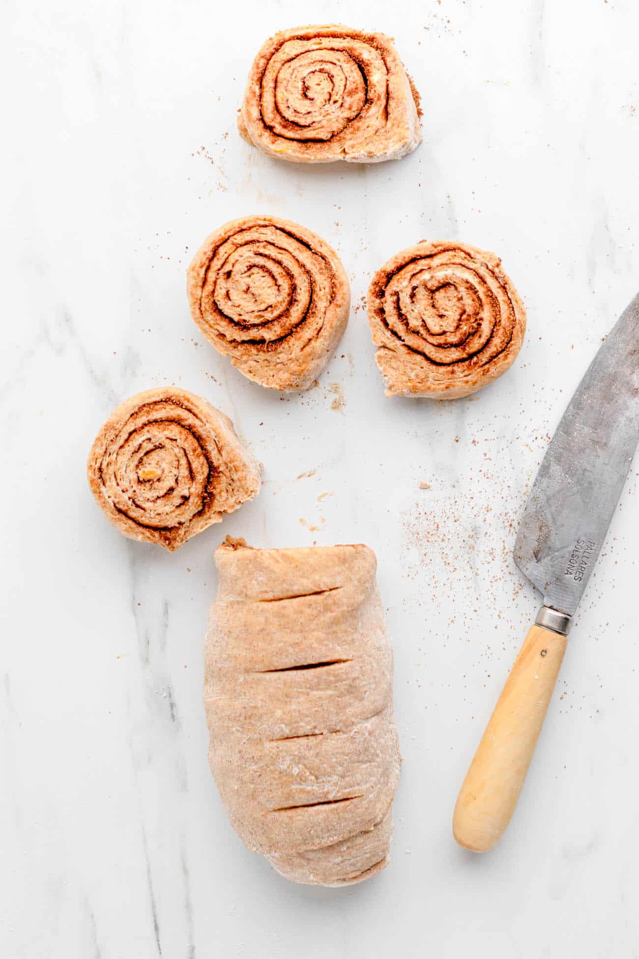 Cinnamon roll dough cut into rolls on a white countertop.