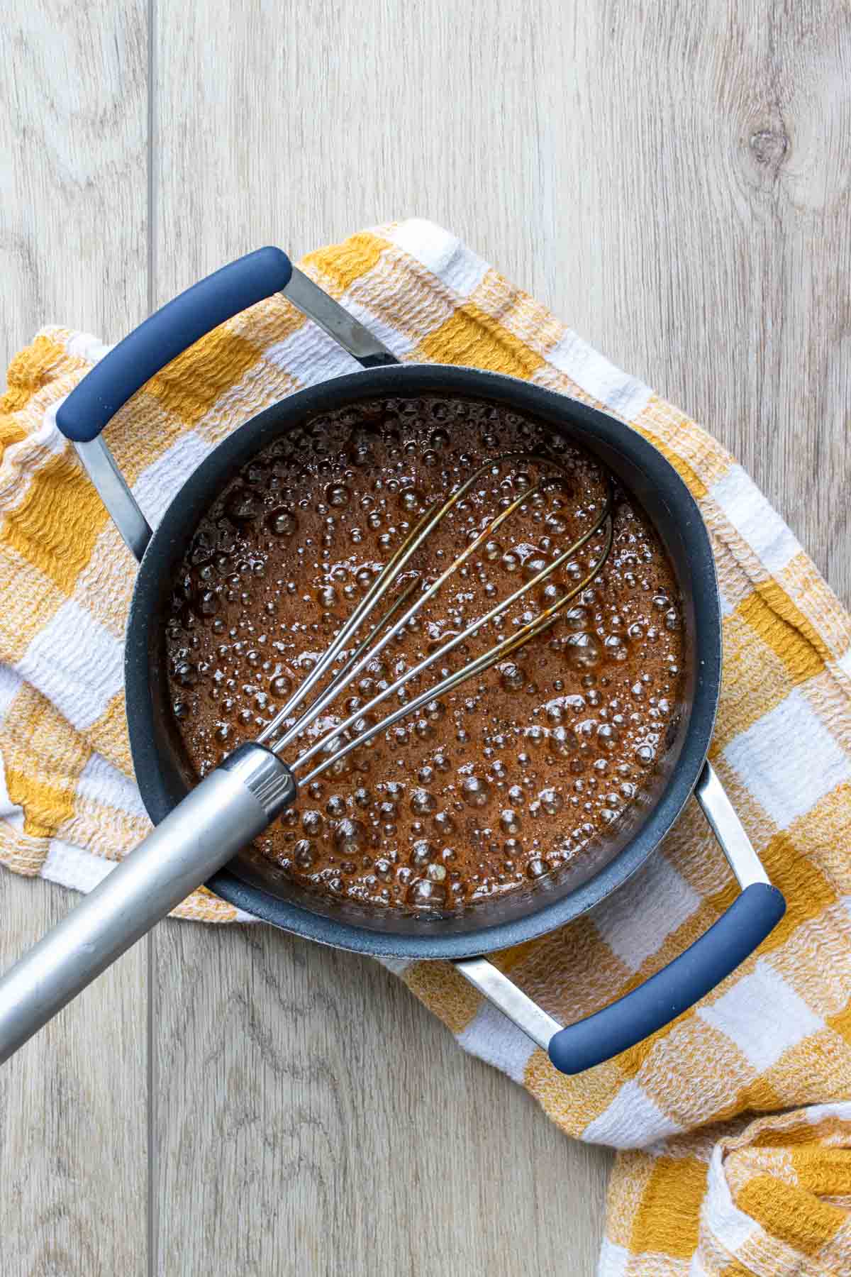 vegan caramel sauce bubbling in pot with a silver whisk