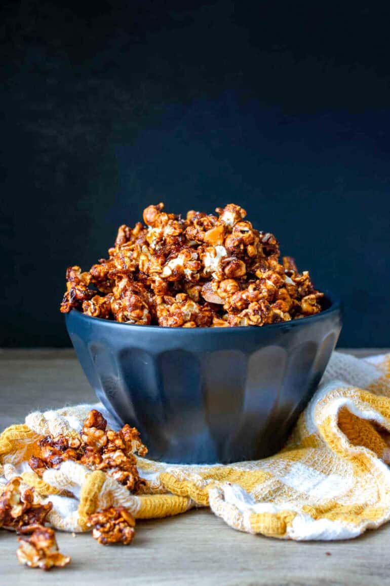 Black bowl overflowing with vegan caramel popcorn sitting on a yellow and white checkered towel.