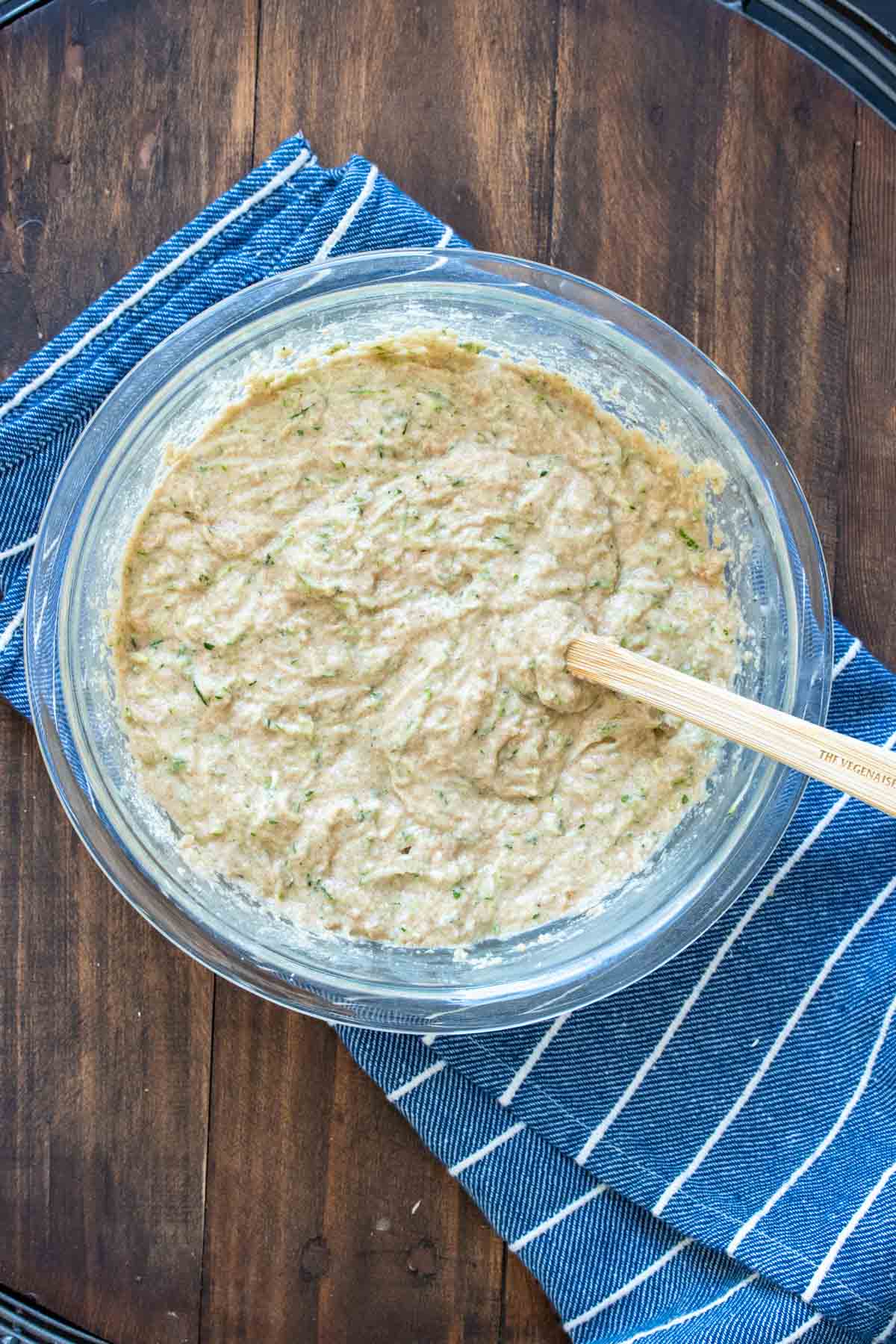 Wet and dry ingredients mixed together in a clear glass bowl with wooden mixing spoon.