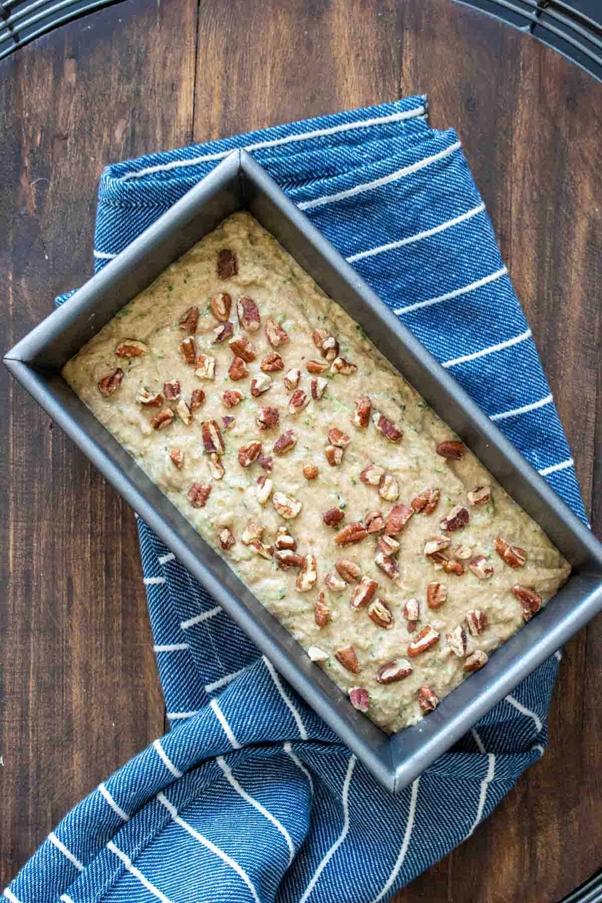 Zucchini bread batter poured into a baking dish, topped with nuts.