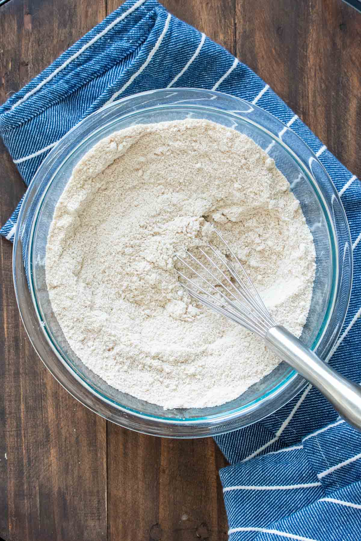 dry ingredients for gluten free zucchini bread in a clear glass bowl with a silver whisk.