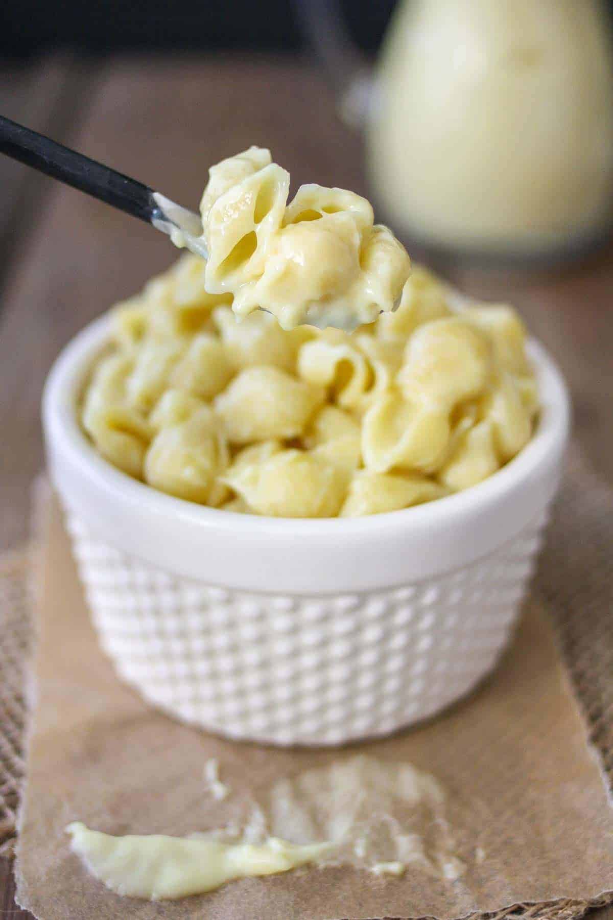 Pasta shells covered with vegan white cheese sauce in a white bowl, with a spoon scooping up some of the pasta. 