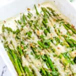 easy cheesy baked asparagus recipe with mozzarella, parmesan and tomatoes in a white baking dish