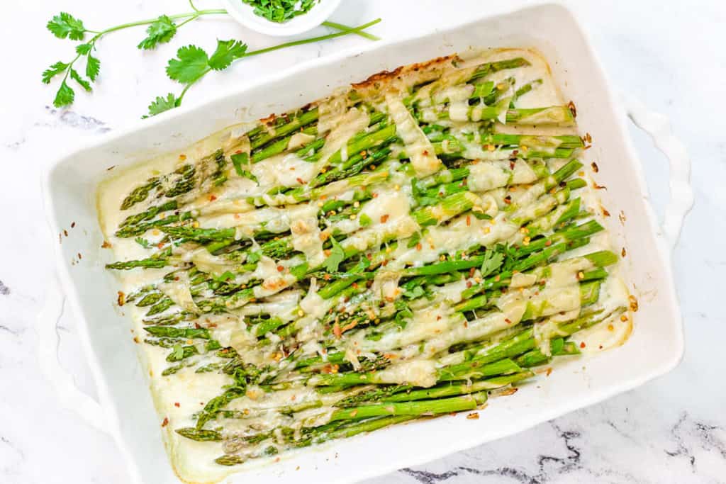 easy cheesy baked asparagus recipe with mozzarella, parmesan and tomatoes in a white baking dish